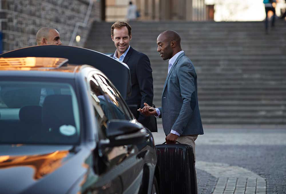 Taxiförare assisterar två affärsmän med resväska