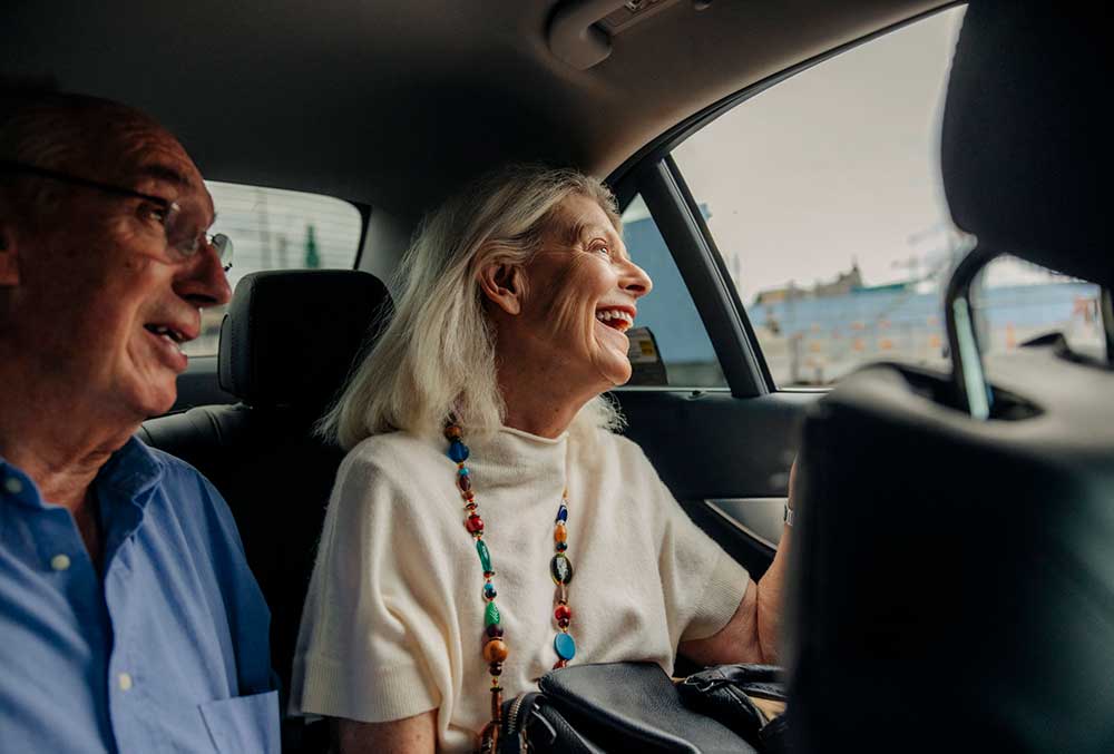 Glad äldre kvinna med sitter i taxi bredvid man, båda ler