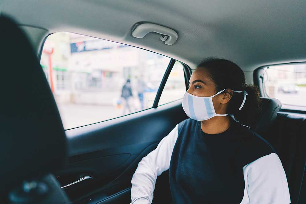 Kvinna bär skyddsmask i en taxis baksäte